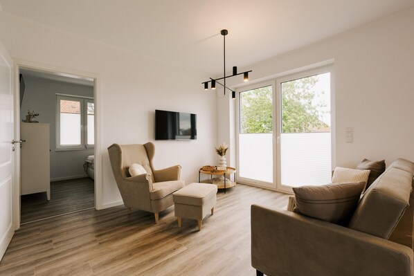 A modern living room with a sofa, armchair, ottoman, and a TV mounted on the wall.