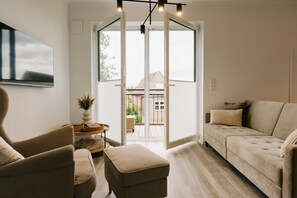 A living room with a sofa, ottoman, and chair, a flat-screen TV, and a sliding glass door leading to an outdoor area.