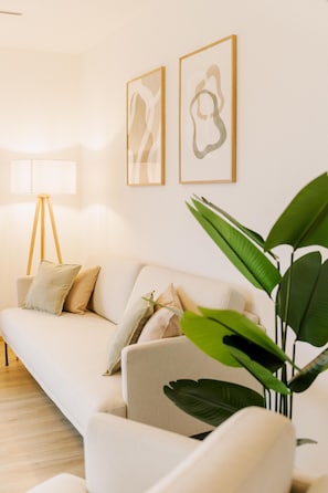 A living room with a sofa, a floor lamp, and two framed artworks on the wall.