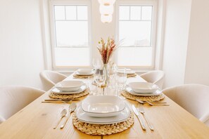 Une table à manger dressée avec des assiettes, des couverts et un vase contenant des plantes séchées.
