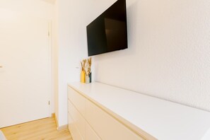 A white wall with a flat-screen TV mounted above a white dresser with drawers. - Canals - Suite 1 | Direct Waterfront Location (Greetsiel)