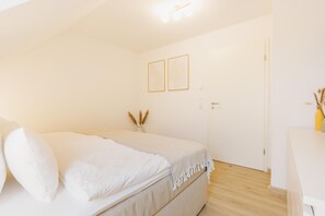 Une chambre à coucher avec un lit, des tables de chevet, une porte et des tableaux encadrés accrochés au mur.
