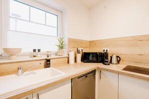 A modern kitchen with a sink, stove, microwave, and coffee maker. - Canals - Suite 1 | Direct Waterfront Location (Greetsiel)