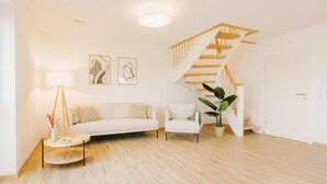 En moderne stue med trappe, sofa, stol, lampe og billedkunst på væggen.