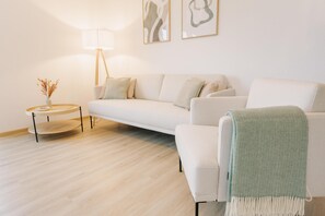 A modern living room with a sofa, a round coffee table, a lamp, and abstract wall art. - Canals - Suite 1 | Direct Waterfront Location (Greetsiel)