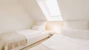 A bedroom with two beds, a skylight, and a bedside table with a lamp. - Canals - Suite 2 | Direct Waterfront Location (Greetsiel)