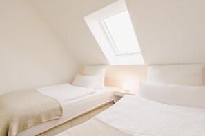 A bedroom with two beds, a skylight, and a bedside table with a lamp. - Canals - Suite 2 | Direct Waterfront Location (Greetsiel)