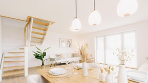 A modern interior with a wooden staircase, a dining area with a wooden table set for four, and a large window providing natural light. - Canals - Suite 2 | Direct Waterfront Location (Greetsiel)