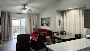 A modern living room with a red sofa, a dining table with chairs, a ceiling fan, and a large window with curtains. - Charming 2-bedroom Penthouse condo with AC, WiFi in lovely BransonMo (Branson)