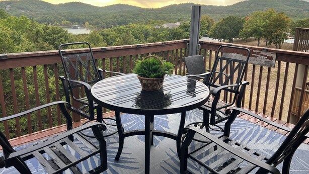 A balcony with a round table and chairs, a potted plant, and a view of a lake and hills. - Charming 2-bedroom Penthouse condo with AC, WiFi in lovely BransonMo (Branson)