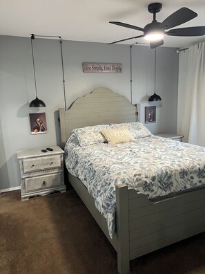Ein Schlafzimmer mit Bett, Nachttischen, Deckenventilator und Wandbildern.