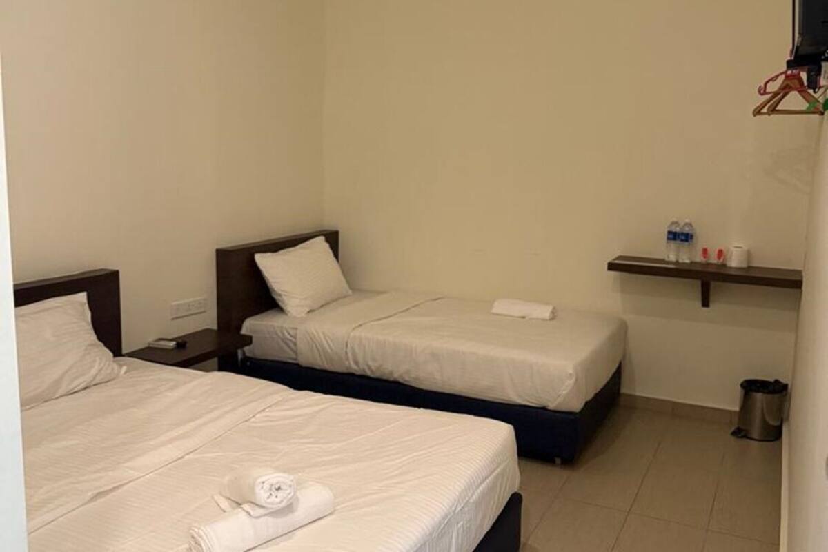 A hotel room with two beds, a small shelf with toiletries, and a trash bin.