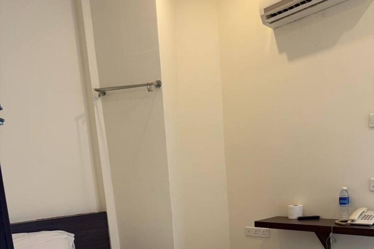 A hotel room with a bed, a small shelf with toiletries, and an air conditioning unit on the wall.