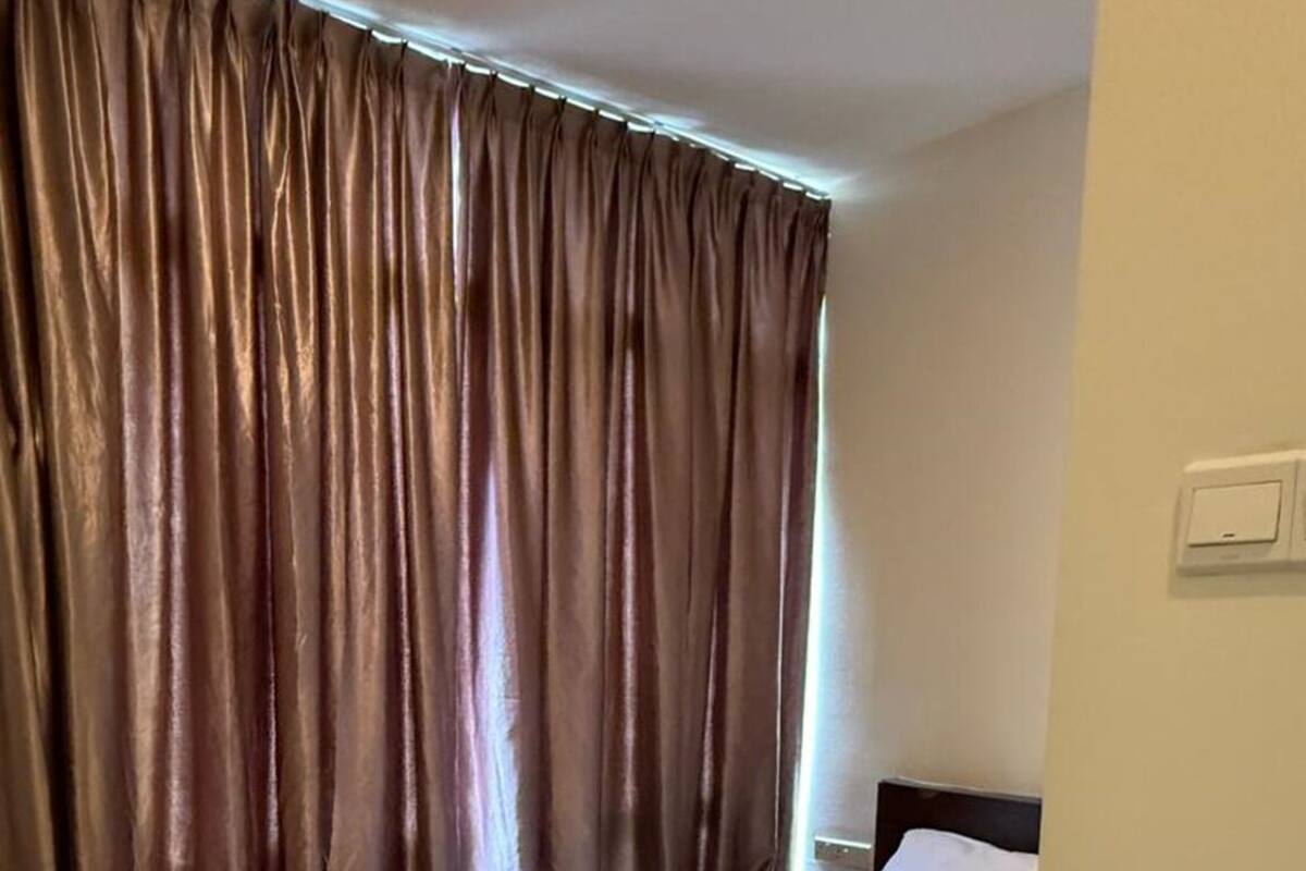 A hotel room with a bed, white linens, a dark headboard, and a curtain.