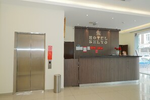 En hotellreception med en bardisk i trä, ett receptionsområde och en hiss.