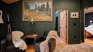 Ein gemütliches Zimmer mit zwei Ledersesseln, einem Holztischchen, einem Landschaftsbild und einem gemusterten Teppich.