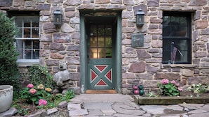 Ein Steinhaus mit grüner Tür, ein kleiner Garten mit rosa Blumen und ein Steinweg, der zum Eingang führt.