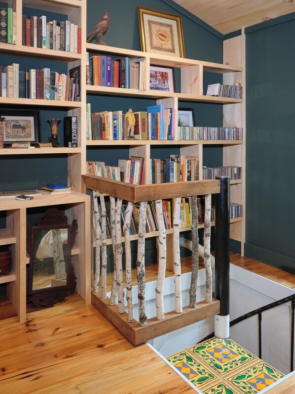 Een bibliotheek met houten boekenkasten vol boeken en CD's, een decoratief houten hekwerk en een vloerkleed met een patroon.