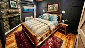 Ein Schlafzimmer mit Steinwand, Kamin, Bett mit Holz Kopfteil, Nachttisch und Deckenventilator.