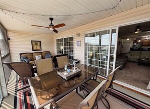 Une terrasse couverte avec une table en verre, des chaises en osier et un ventilateur de plafond.