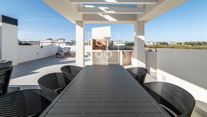 Une terrasse sur le toit avec une longue table et des chaises, une pergola offrant une vue panoramique et un paysage urbain en arrière-plan.