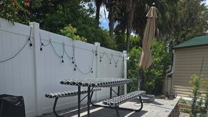 Une terrasse avec un sol en pierre, une clôture blanche et une table recouverte d’une nappe à motifs.