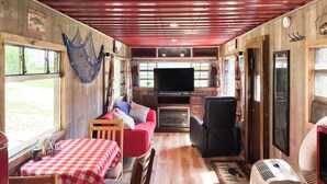 Un interior acogedor con suelo de madera, una mesa a cuadros rojos y blancos, un sofá, un televisor y una hamaca.