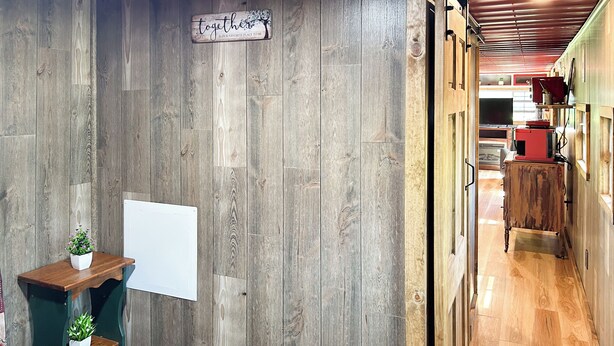 Una habitación con paredes de madera, una cama con colcha a cuadros rojo y negro, una pequeña mesa de madera con una planta en maceta y un letrero que dice 'Juntos es nuestro lugar favorito'.