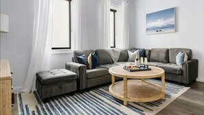 A modern living room with a grey sectional sofa, a round coffee table, and a large window with white curtains. - 4 Bedroom - 4 Blocks to King St. with Parking (Charleston)