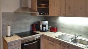 Une cuisine compacte équipée d’une cuisini ère, d’un four et d’un évier, de placards en bois et d’une machine à café.