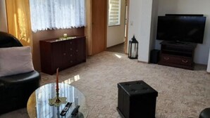 Un salon avec un canapé, une table basse en verre sur laquelle est posée une bougie, un téléviseur et un meuble.