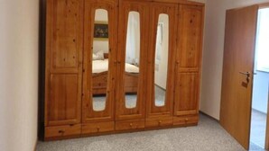 Une armoire en bois avec des portes miroir, dans une pièce dont le sol est recouvert de moquette et qui possède une porte sur le côté droit.