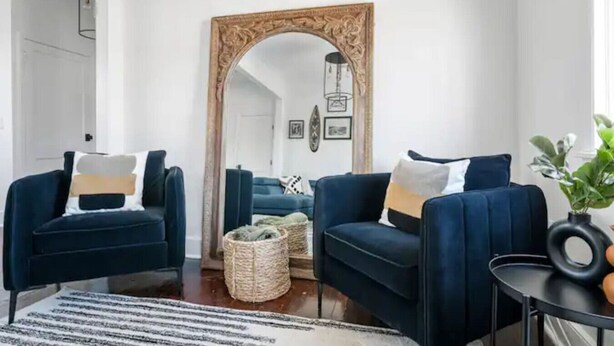 Una sala de estar con dos sillones azul oscuro, un espejo grande y una mesita auxiliar con una planta.