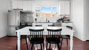 Una cocina moderna con armarios blancos, un refrigerador de acero inoxidable, un horno empotrado y un comedor con mesa blanca y sillas negras.