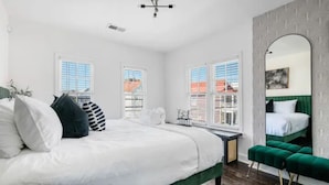 Un dormitorio moderno con una cama grande, un banco tapizado en verde y un espejo amplio.