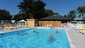 Une piscine avec des personnes dedans, entourée de chaises longues et délimitée par une clôture.