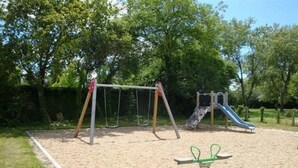 Une aire de jeux avec des balançoires, un toboggan et une bascule.