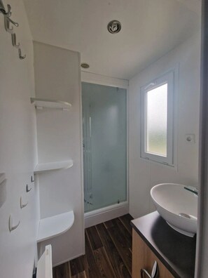 Ein Badezimmer mit einer gläsernen Duschkabine, einem weißen Waschbecken und einem Fenster.