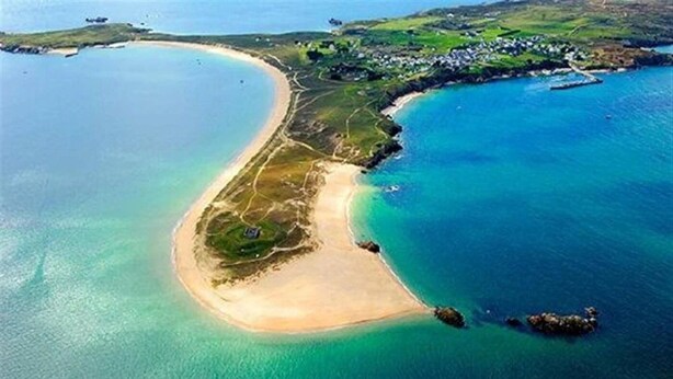 Vue aérienne d’une zone côtière avec une plage de sable, des eaux d’un bleu limpide et un petit village composé de maisons.