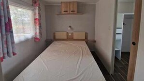 Une petite chambre avec un lit simple, une tête de lit en bois, une table de chevet et une fenêtre avec des rideaux.