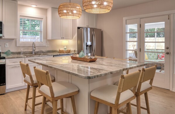 A kitchen with a central island, bar stools, a refrigerator, and a window with blinds.