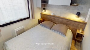 Une chambre à coucher comprenant un lit, des tables de chevet, une commode, une fenêtre avec des rideaux, une étagère fixée au mur et un luminaire fixé au mur.