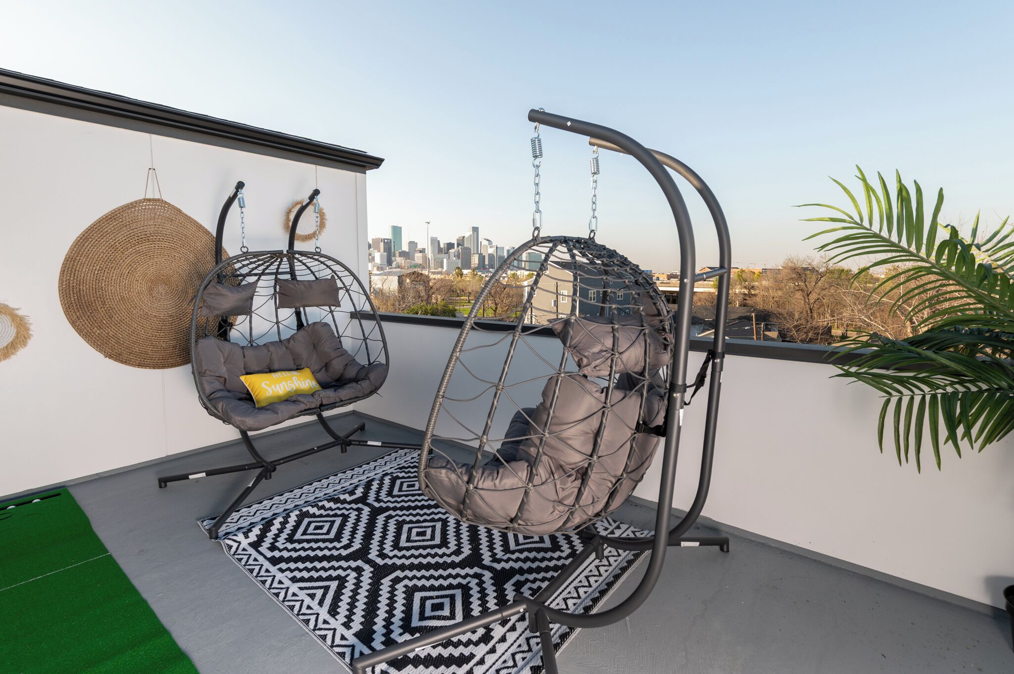 Ein Balkon mit zwei Hängestühlen, einem gemusterten Teppich und Blick auf eine Stadtlandschaft.