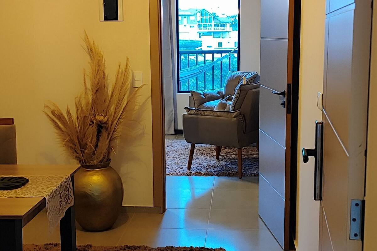 Ein modernes Interieur mit Holzboden, einem Essbereich mit Tisch und Stühlen, einer dekorativen Vase und Blick auf einen Balkon mit Gartenmöbeln.