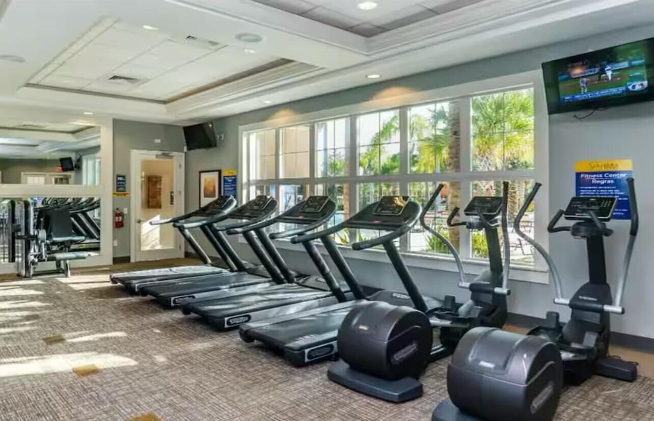 A gym with treadmills, ellipticals, and a TV on the wall.