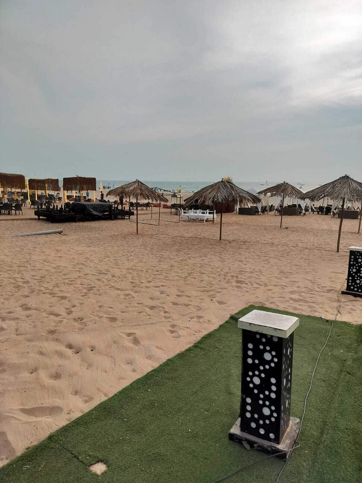 Une plage avec des parasols en chaume et des chaises longues, une zone herbeuse et un élément décoratif aquatique.