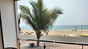 A balcony with a view of a beach, a palm tree, and two wicker chairs. - Surf House Beach Resort (Baga)
