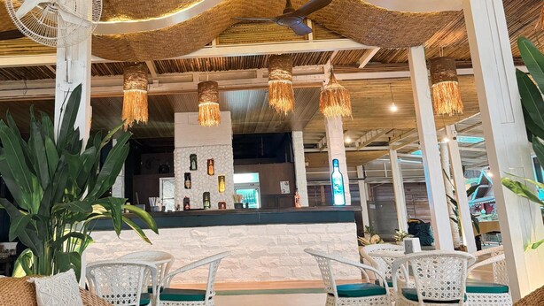 A cozy indoor seating area with wicker furniture, a glass-top table, and a bar counter in the background. - Surf House Beach Resort (Baga)