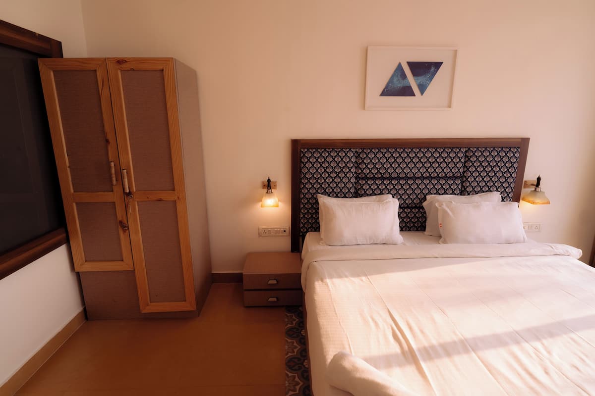A bedroom with a bed, a wardrobe, a nightstand, and a wall-mounted light fixture.