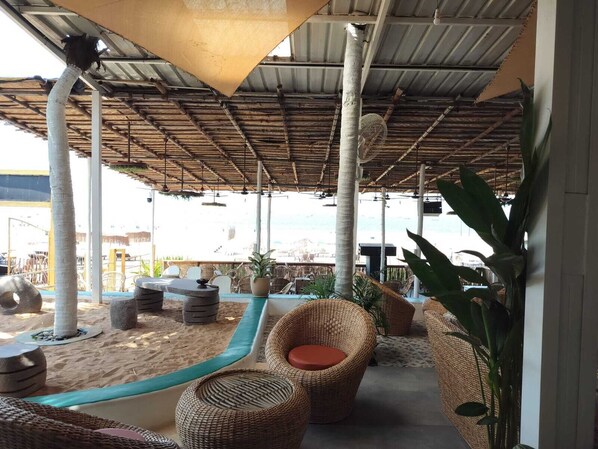 Un área de estar al aire libre con mobiliario de mimbre, una fuente de agua y vista a la playa.